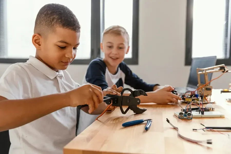 Enfants manipulant une pince robotique parmi des composants électroniques sur une table